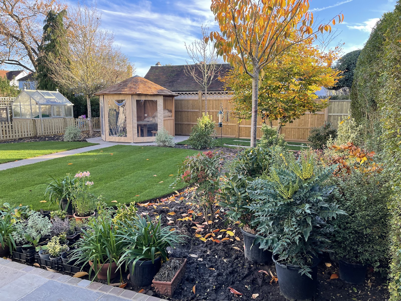 An autumn garden with a corner summerhouse, a manicured lawn and freshly planted mixed borders coming into their own along the boundary.